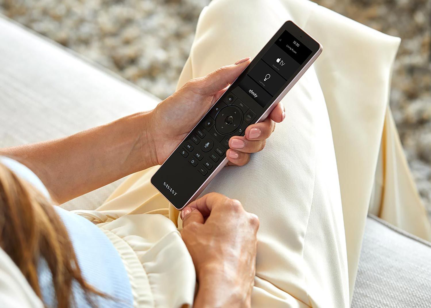 Person holding a Savant remote control while seated on a sofa